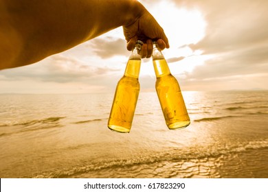 Hand Holding A Bottles Of Beer On The Beach At Sunset Time