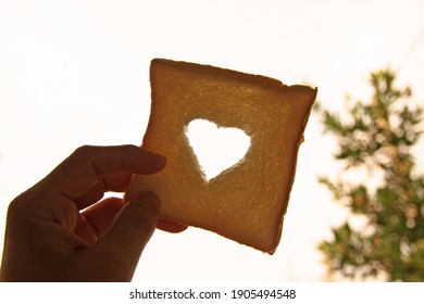 Hand Holding Bread Slice With Heart Shaped Hole Isolated.