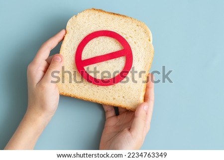 Hand holding a Bread slice marked with sign prohibited. Wheat allergy background 