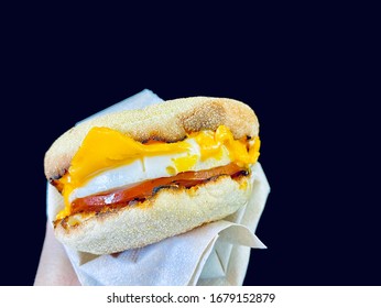 Hand Holding Breakfast Sandwich With Egg Ham Bacon And Cheese On Toasted English Muffin Held