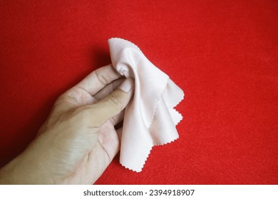 A hand holding a brightly colored cloth that serves to wipe glasses, on a red background - Shutterstock ID 2394918907