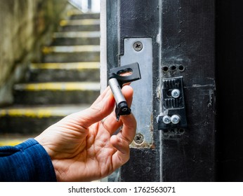 Hand Holding Broken Striking Plate From A Residential Or Commercial Fire Exit Door. Damage To Door Frame And Strike Plate From Thieves / Burglars Using A Crowbar. Soft Bokeh Stair Backround. 