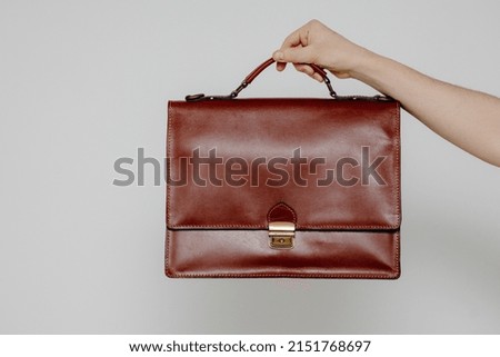 Hand holding a brown briefcase, Brown Vintage leather briefcase with strap and brass buckle.