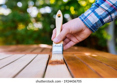 Hand Holding A Brush Applying Varnish Paint On A Wooden Garden Table - Painting And Caring For Wood With Oil