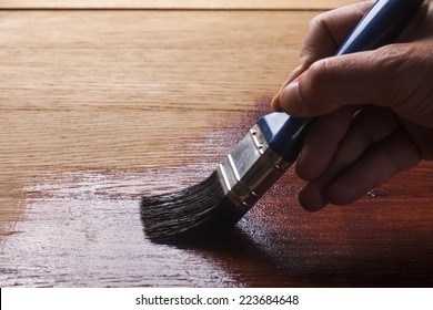 hand holding a brush applying  varnish paint  on a wooden surface