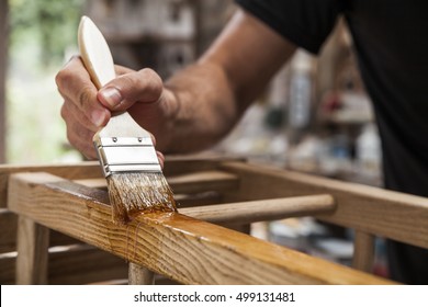 Hand, die eine Bürste hält, die eine lackierte Farbe auf Holzmöbeln anbringt
