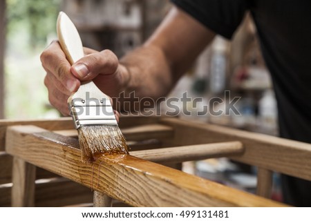 hand holding a brush applying varnish paint on a wooden furniture