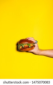 Hand Holding Burger Against Yellow Background