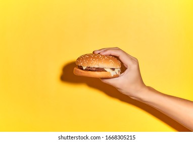 Hand Holding Burger Isolated On Light Yellow Background .studio Shot.