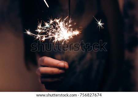 hand holding a burning firework bengal light. space for text. burning sparkler closeup in female hand in dark. happy new year and merry christmas concept. happy holidays