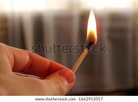 Hand holding a burning match. Match with fire and flame on a dark background. The concept of arson and fire. A burning match in his hand. Arson. Ignition of pyrotechnics. Matches and children.