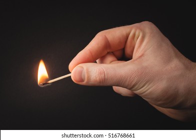 Hand holding burning match stick. Photo on a black background