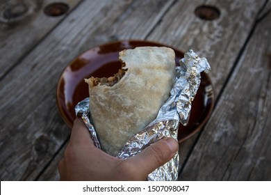 Hand Holding A Burrito With A Bite Out Of It In California