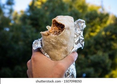 Hand Holding A Burrito With A Bite Out Of It In California