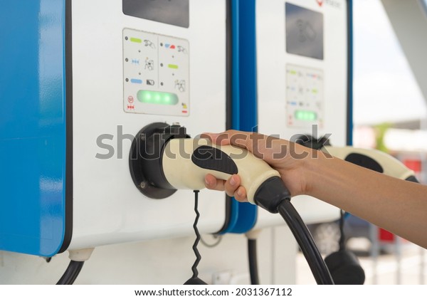 A hand holding cables from EV car charger or\
electric vehicle station. Cable connected at gas station, power\
supply battery charging an alternative eco environment future\
technology energy innovation