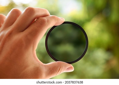Hand holding camera lens filter. Polarizing filter - photography accessories. Green nature background.