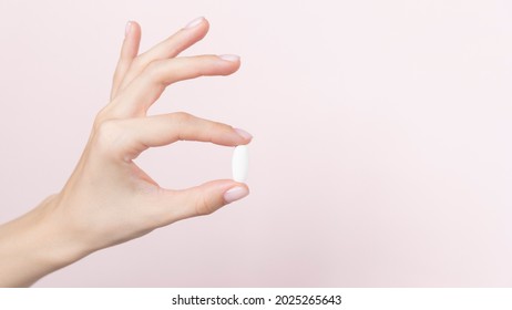 Hand holding a capsule or pill on a pink background. High quality photo