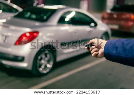 Hand holding a car alarm key with anti-theft. businessman closes his expensive gray car in an underground parking lot