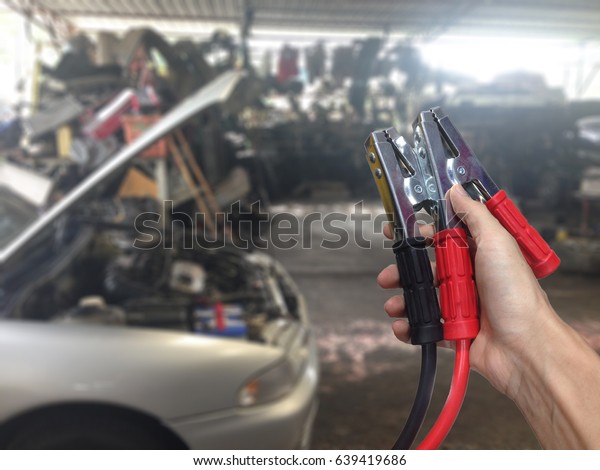 Hand holding Car battery charger over blurred\
car in garage background.