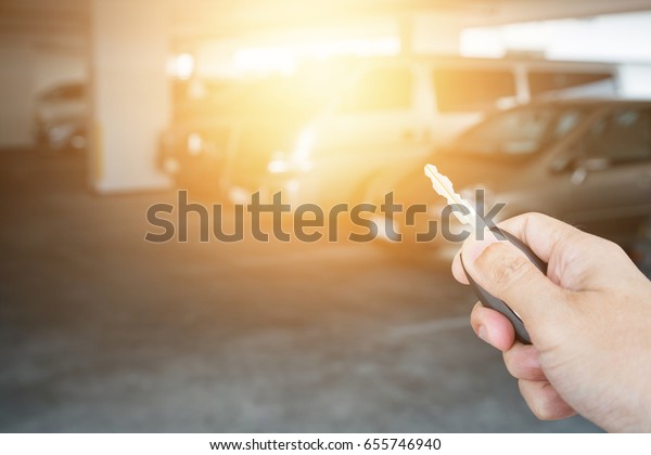 Hand\
holding car key remote at car park\
background