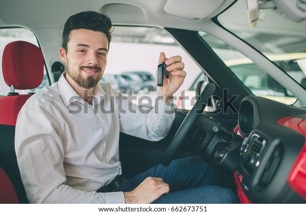 Hand holding car key remote,\
with modern car backgrounds. man sitting inside new car with\
keys.