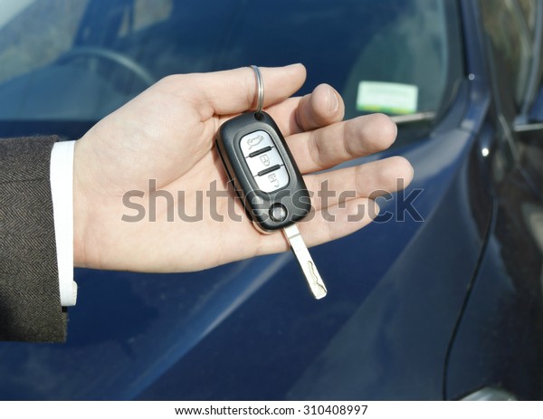 Hand holding car key for starting the
car.Male hand with car key on car background
