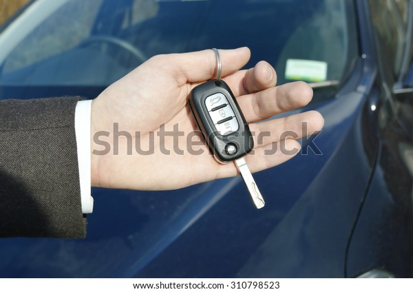 Hand holding car key for starting the\
car.Male hand with car key on car background\
