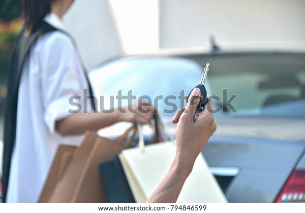 Hand holding car keys remote with\
blurred happy  young woman carrying many colourful shopping bags in\
the car park. LetÃ¢â?¬â?¢s go to shoes store\
more.