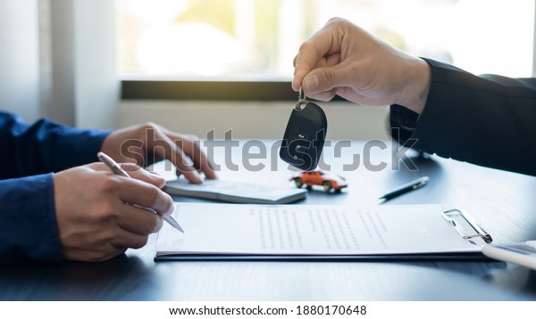 Hand holding car keys and car\
rental concept A close-up view of the agent, giving the customer\
the car keys after signing the lease, rental form and car\
name.