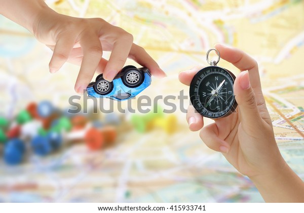 hand holding car model with blur\
pile of pins on map background ,transportation\
concept