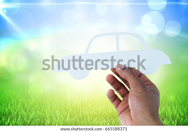 hand holding a car in paper against grass under a\
sunny sky