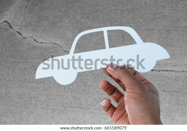 hand holding a car in paper against concrete wall\
with crack