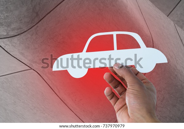 hand holding a car in paper against view of\
building exterior