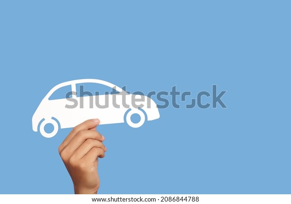 Hand holding car paper cut model\
on blue  background. Cost of car concept.Car\
Insurance.