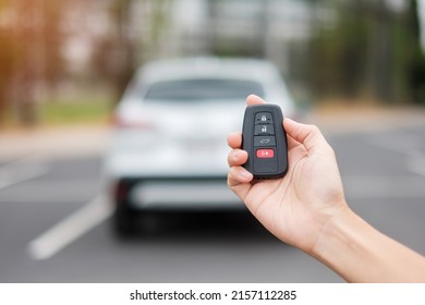 Hand holding car remote control, smart key to lock or unlock doors of white car. Safety, travel and transportation concept