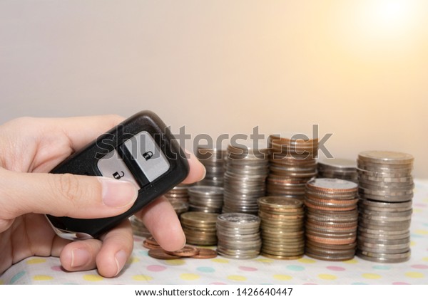 Hand holding a car\
remote control with coin stacks, concept of insurance,loan,finance\
and buying car