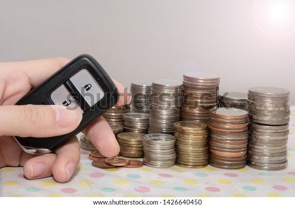 Hand holding a car\
remote control with coin stacks, concept of insurance,loan,finance\
and buying car