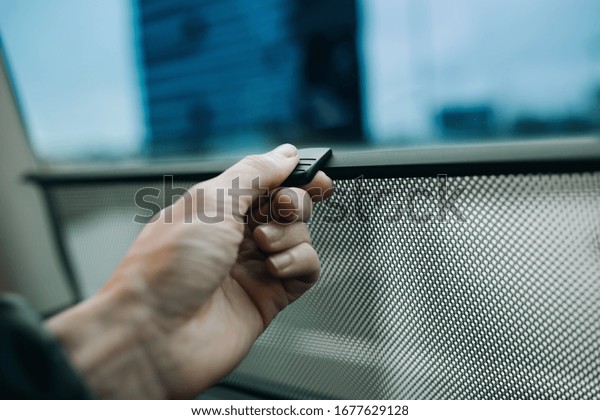 Hand is holding car side window curtains sunshades.\
Insect screen at the car
