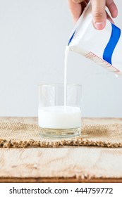 Hand Holding A Carton Of Milk Poured Into A Glass On White Background