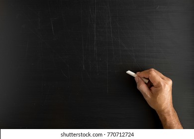 Hand holding a chalk and writing something against blackboard with copy space on blackboard.
