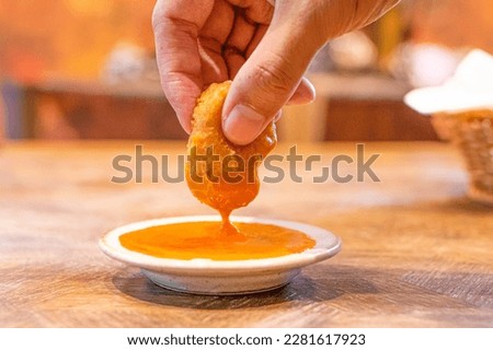 Hand holding a chicken nugget and dipping in spicy chili sauce