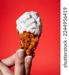 Hand holding a chicken wing with buffalo and ranch dressing on a red background.