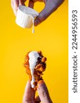 Hand holding a chicken wing with buffalo and ranch dressing on a yellow background.
