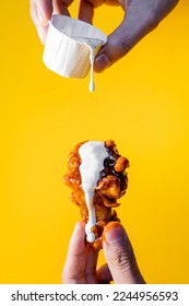 Hand holding a chicken wing with buffalo and ranch dressing on a yellow background. - Shutterstock ID 2244956593