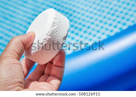 Hand holding Chlorine Pellets with inflatable pool on background