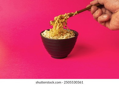 Hand Holding Chopsticks Lifting Ramen Noodles from Black Bowl against Pink Background - Powered by Shutterstock