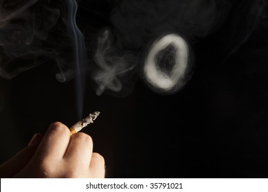 Hand Holding Cigarette With Smoke Ring On Black Background