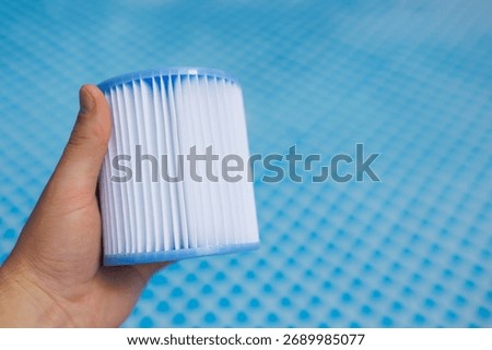 Hand holding clean pool filter cartridge against blue background
