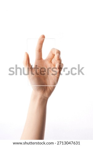 Hand holding a clear, empty rectangular object against a white background in a bright setting during daylight