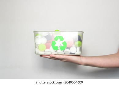 Hand holding a clear plastic recycling box filled with bottle caps. Recycle logo in green color. Solidarity Bottle Caps Concept.